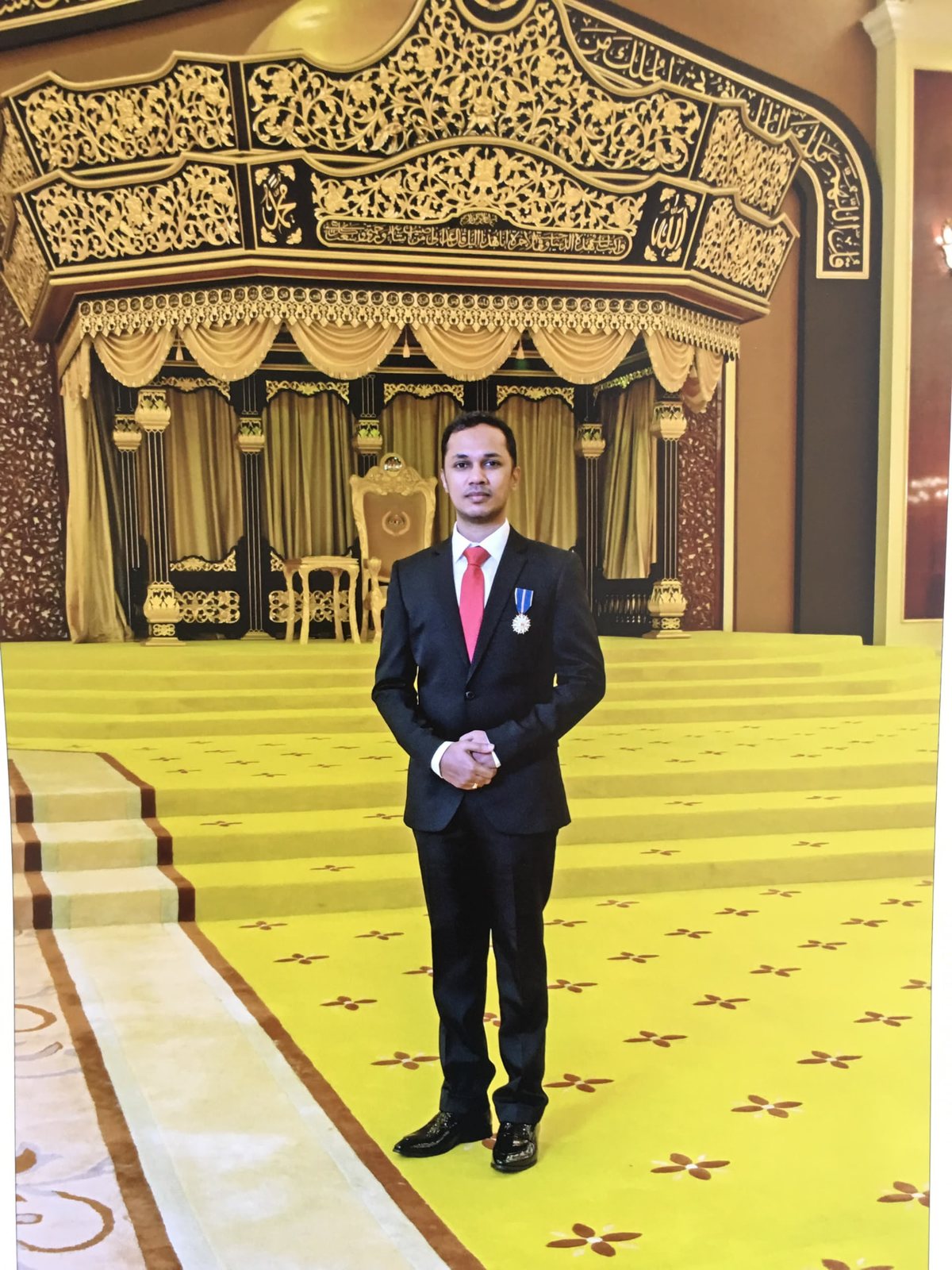 Mr Kumaraveelu standing in the throne room of Istana Negara wearing the A.M.N. medal